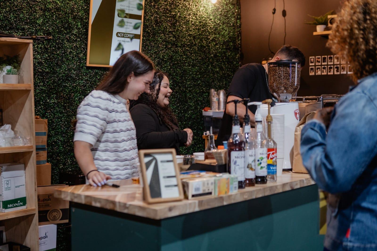 Two volunteers behind the café counter cracking up while drinks are made