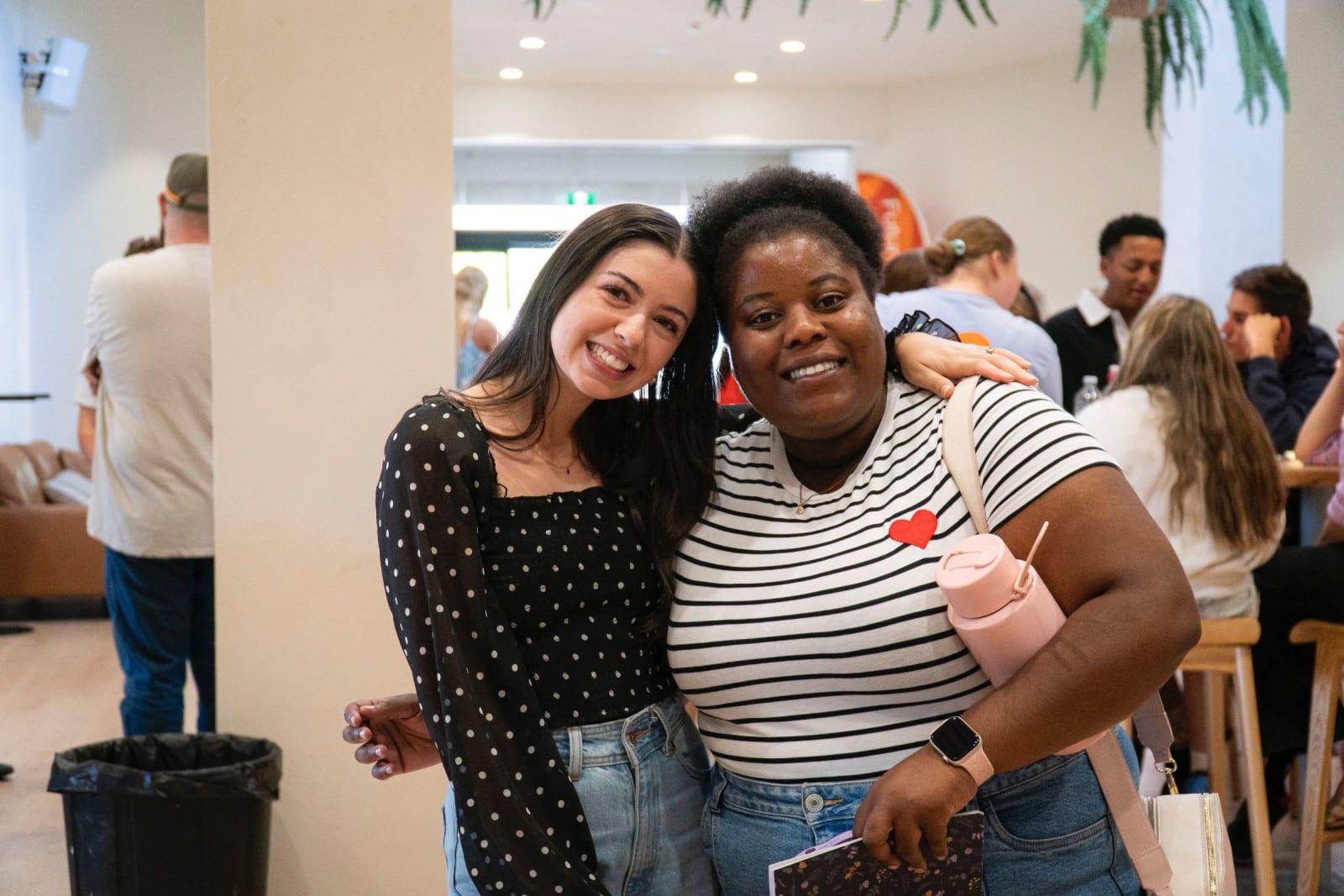 Two friends arm in arm, beaming in the lobby after the service
