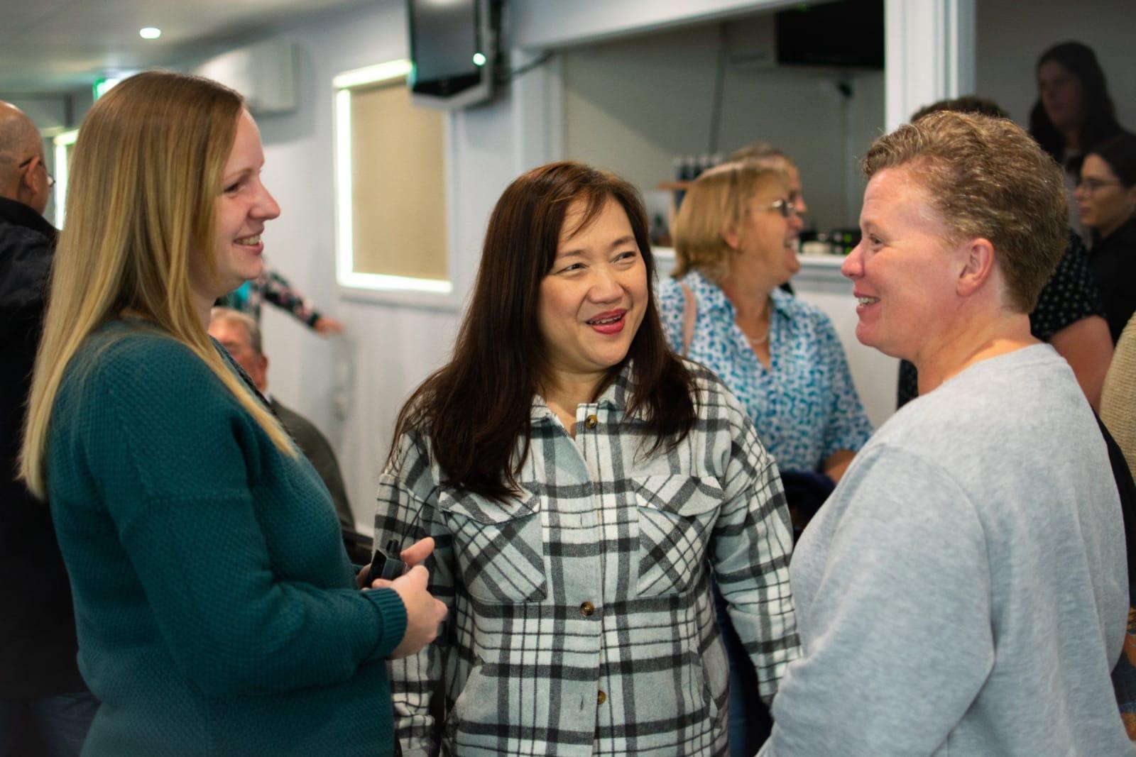 Three women mid-laugh in conversation in the bright foyer