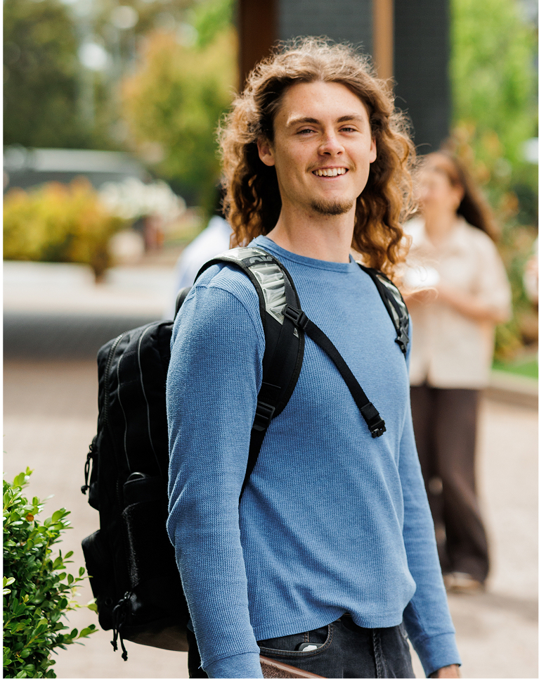 A student smiling outdoors with a backpack